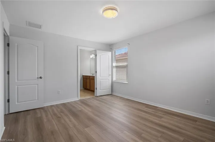 Unfurnished bedroom with baseboards, ensuite bath, visible vents, and light wood finished floors