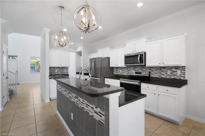 Kitchen featuring light tile patterned floors, hanging light fixtures, a kitchen island with sink, stainless steel appliances, and white cabinetry