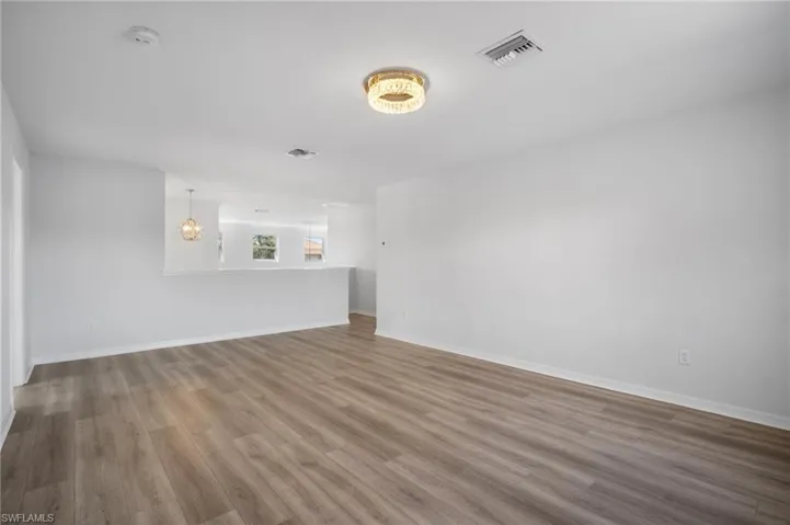 Unfurnished living room with an inviting chandelier, visible vents, baseboards, and wood finished floors
