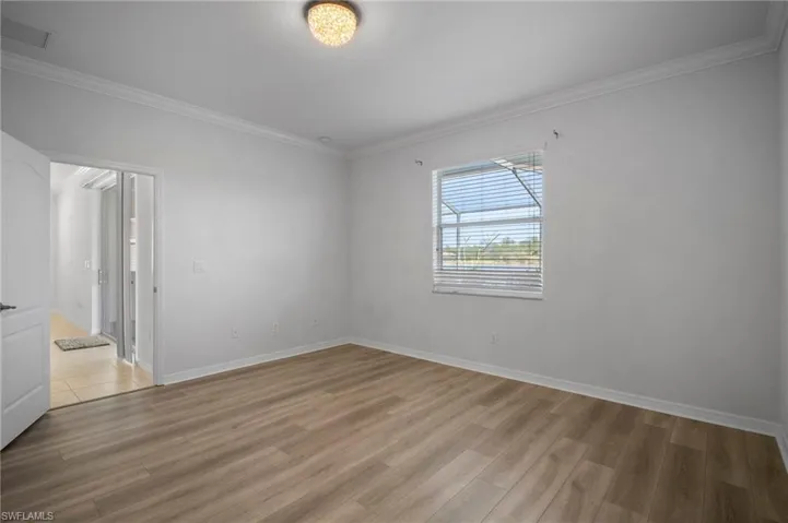 Empty room featuring visible vents, crown molding, light wood-style flooring, and baseboards