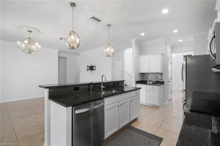 Kitchen featuring a kitchen island with sink, stainless steel appliances, a sink, and white cabinetry