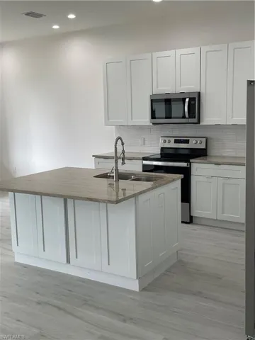 Kitchen featuring sink, white cabinets, light stone countertops, range, and tasteful backsplash