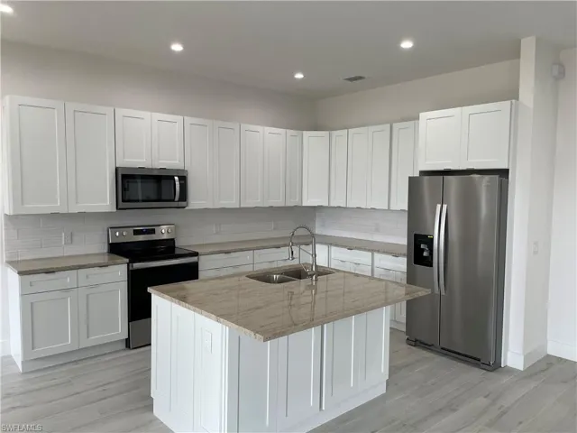 Kitchen featuring sink, white cabinets, stainless steel appliances, and an island with sink