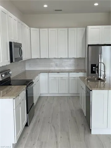Kitchen with white cabinetry, refrigerator, range, dishwashing machine, and light stone countertops