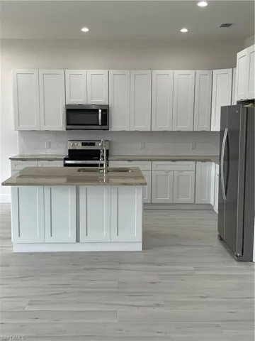Kitchen featuring refrigerator, white cabinetry, stove, an island with sink, and sink