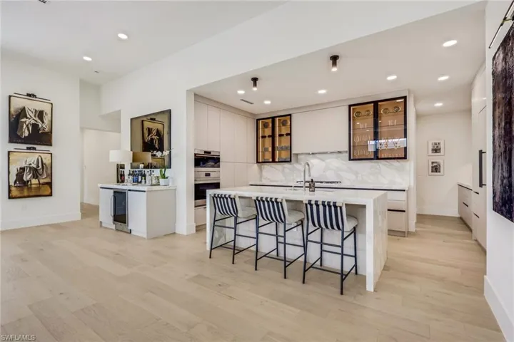 Kitchen featuring a center island with sink, glass insert cabinets, light wood-style flooring, a kitchen breakfast bar, and recessed lighting