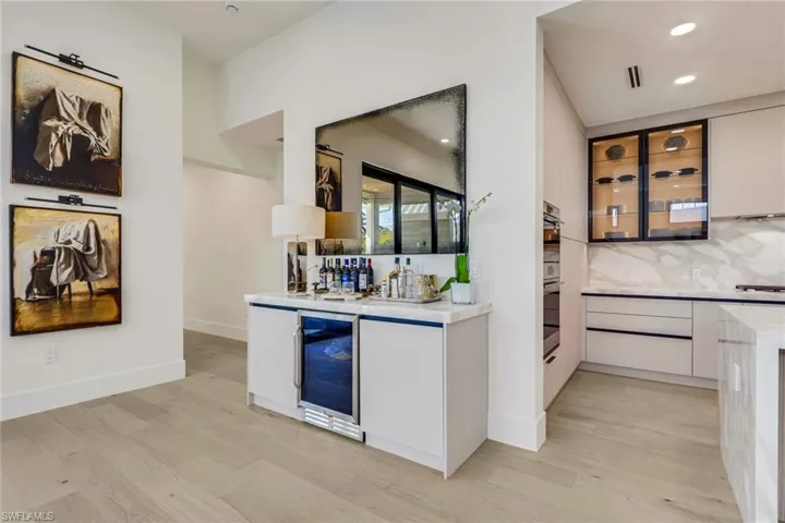 Indoor dry bar featuring light stone countertops, modern cabinets, glass insert cabinets, light wood finished floors, and wine cooler