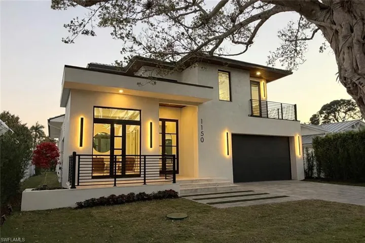 Contemporary house featuring an attached garage, stucco siding, driveway, a balcony, and a front lawn