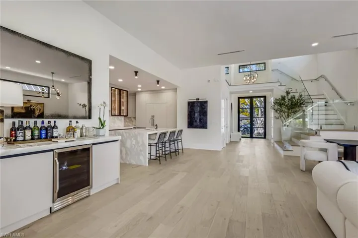 Indoor wet bar with beverage cooler, light wood-type flooring, white cabinetry, and light stone countertops