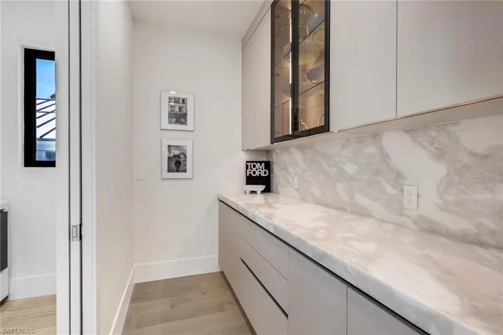 Bar with modern cabinets, light stone counters, light wood finished floors, tasteful backsplash, and glass insert cabinets