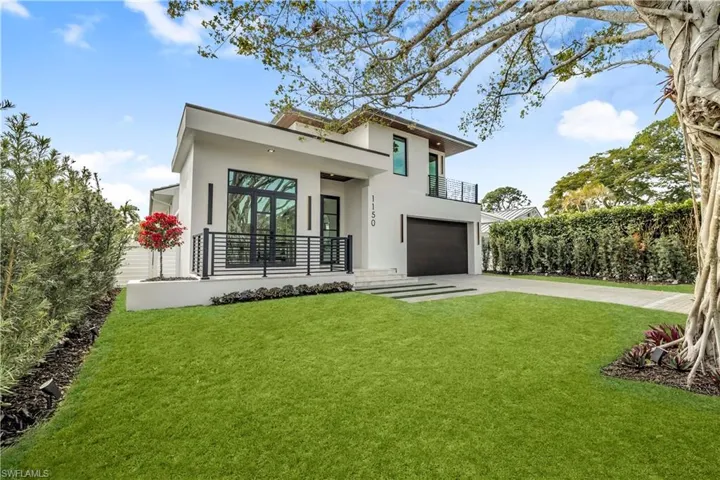 Rear view of property featuring stucco siding, an attached garage, driveway, and a yard
