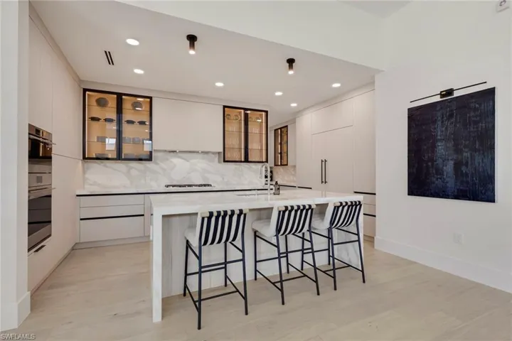 Dual tone kitchen featuring a breakfast bar area, modern cabinets, light stone countertops, light wood finished floors, and recessed lighting