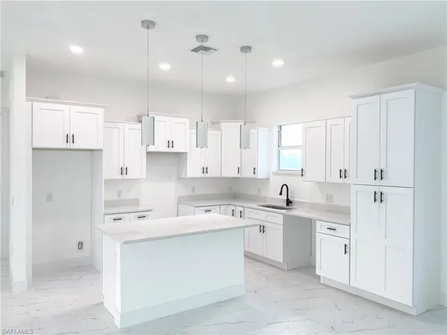 Kitchen featuring hanging light fixtures, a kitchen island, and white cabinets