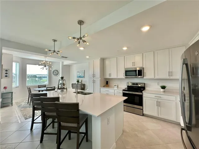 Kitchen featuring an island with sink, white cabinets, pendant lighting, and appliances with stainless steel finishes.