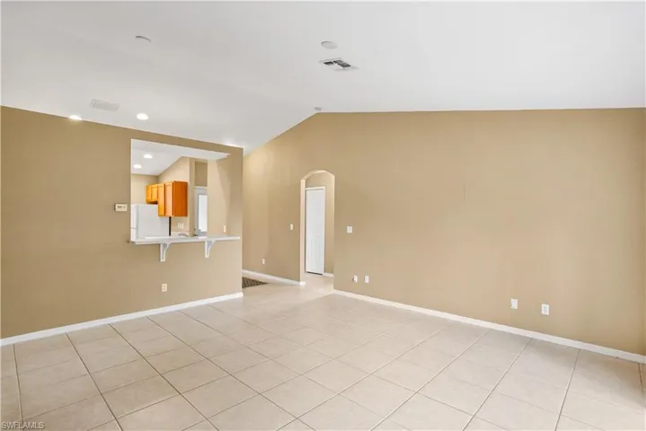 Empty room with vaulted ceiling and light tile flooring