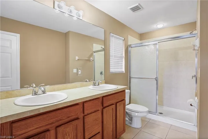 Bathroom with oversized vanity, toilet, tile floors, walk in shower, and double sink