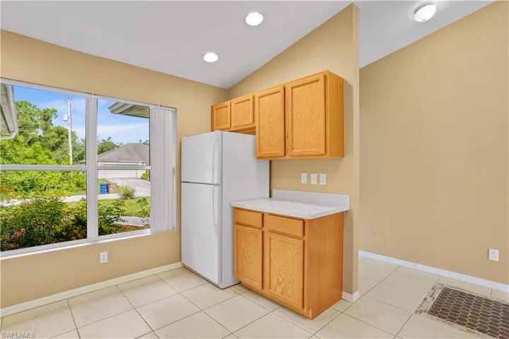 Kitchen featuring vaulted ceiling, plenty of natural light, white fridge, and light tile flooring