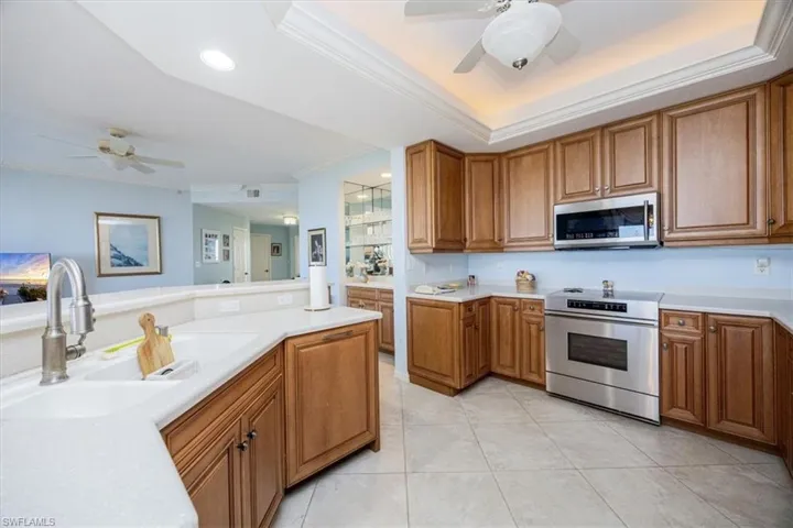 Kitchen featuring crown molding, sink, light tile patterned floors, appliances with stainless steel finishes, and a tray ceiling