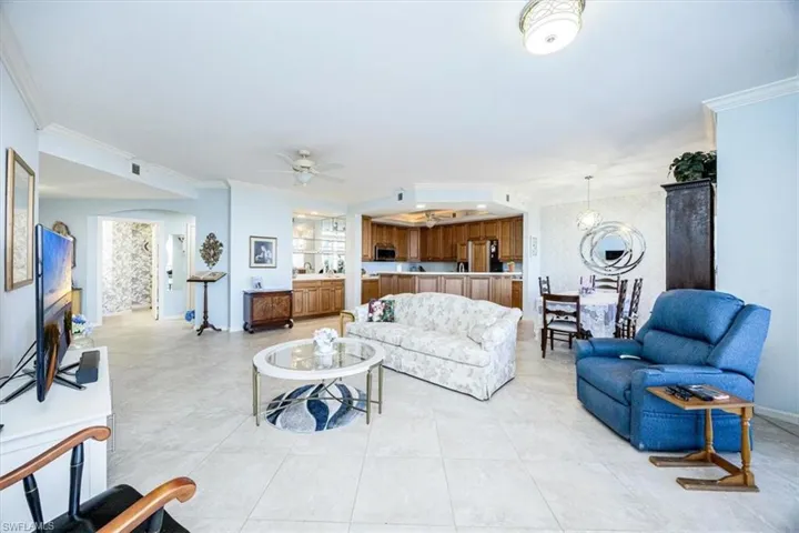 Living room featuring crown molding, a fireplace, light tile patterned floors, and ceiling fan with notable chandelier