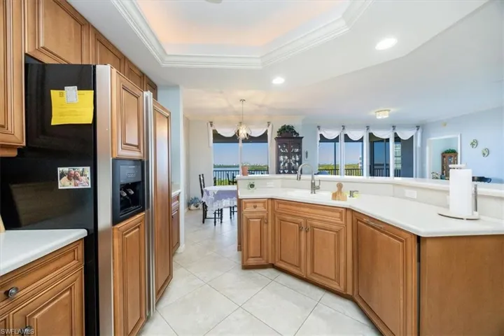 Kitchen with a tray ceiling, fridge with ice dispenser, crown molding, and a notable chandelier
