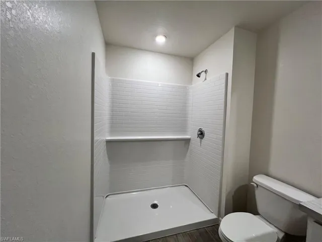 Full bath with a shower stall, a textured wall, and dark wood finished floors