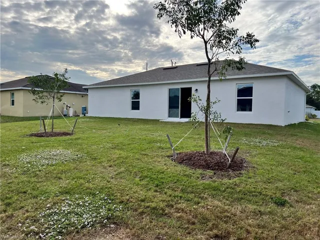 Rear view of property featuring stucco siding, a lawn, and roof with shingles