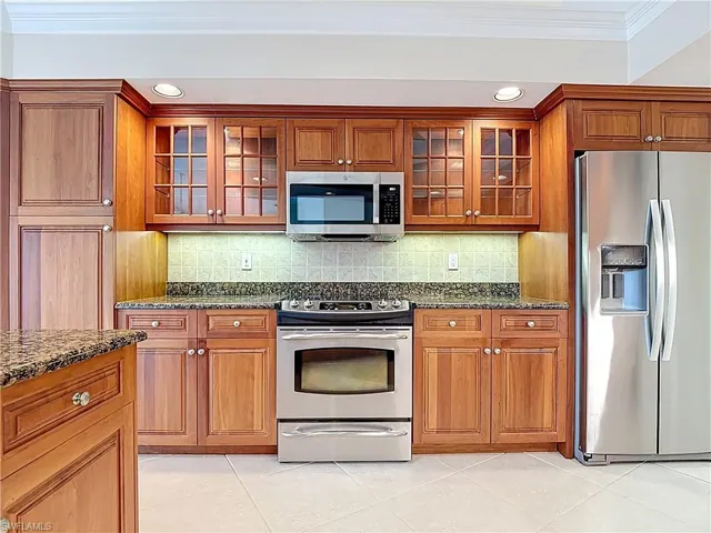 Kitchen with stainless steel appliances, crown molding, light tile patterned floors, dark stone countertops, and recessed lighting