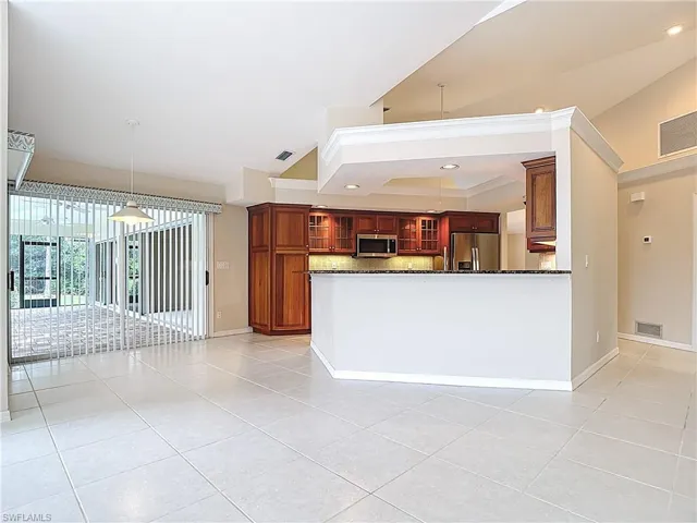 Kitchen featuring light tile patterned floors, dark stone countertops, vaulted ceiling, stainless steel appliances, and glass insert cabinets
