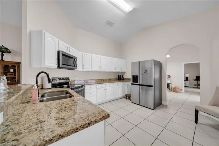 Kitchen with light stone countertops, stainless steel appliances, arched walkways, white cabinets, and vaulted ceiling