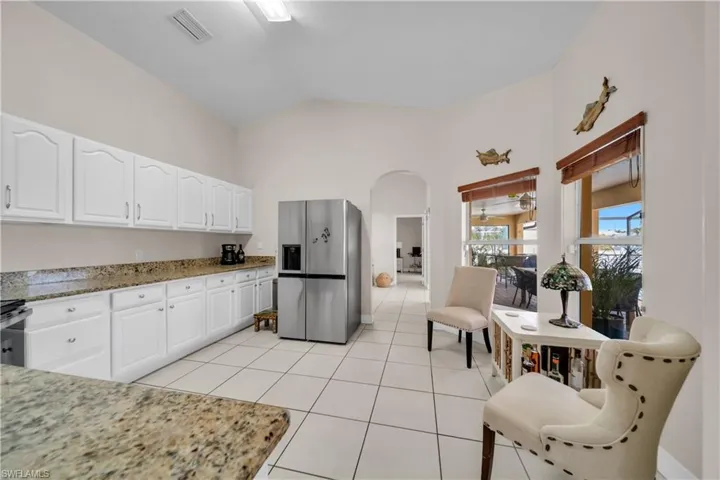 Kitchen featuring light stone countertops, stainless steel appliances, arched walkways, white cabinets, and light tile patterned floors