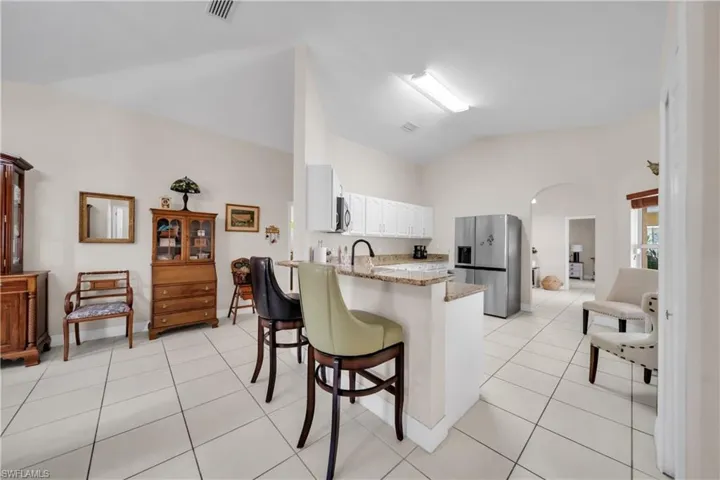 Kitchen featuring stainless steel appliances, white cabinets, vaulted ceiling, arched walkways, and a breakfast bar area