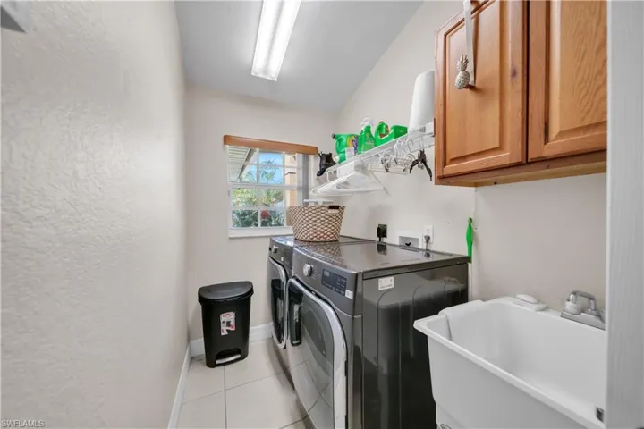 Laundry area with washing machine and clothes dryer, cabinet space, light tile patterned floors, and a textured wall
