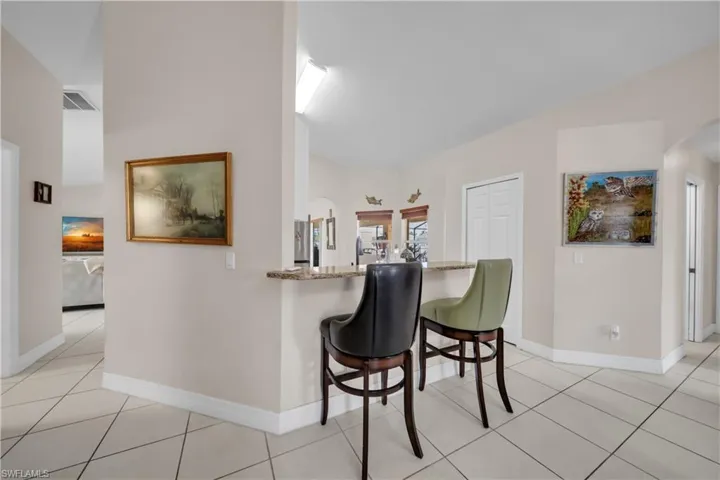 Kitchen with arched walkways, a kitchen breakfast bar, vaulted ceiling, light tile patterned flooring, and light stone countertops