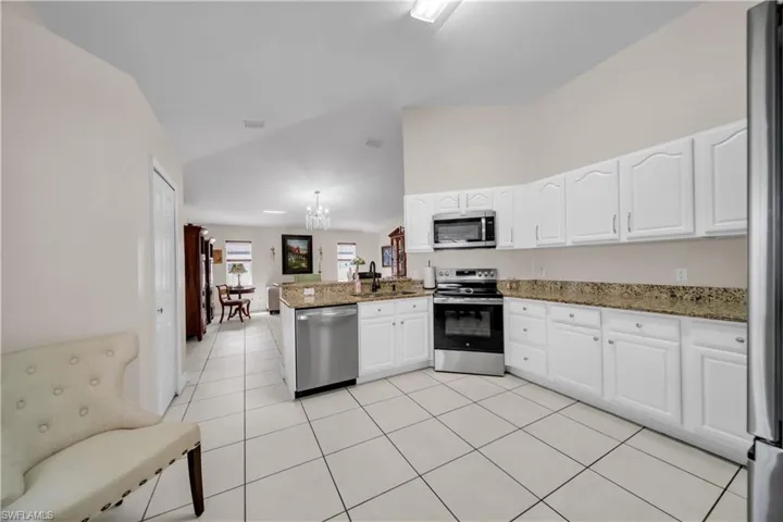 Kitchen with stainless steel appliances, a peninsula, dark stone counters, white cabinetry, and light tile patterned floors