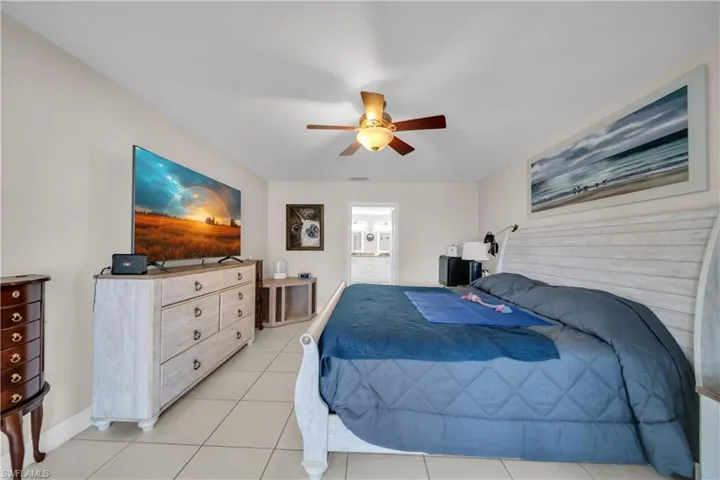 Bedroom with ceiling fan, light tile patterned floors, and connected bathroom