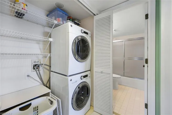 Laundry area with light tile patterned flooring and stacked washer / dryer