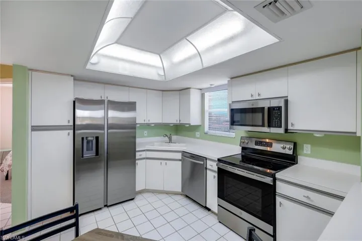 Kitchen with sink, stainless steel appliances, white cabinetry, and light tile patterned floors