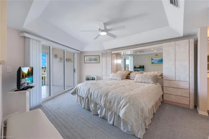 Bedroom with a raised ceiling, light colored carpet, ceiling fan, and access to exterior