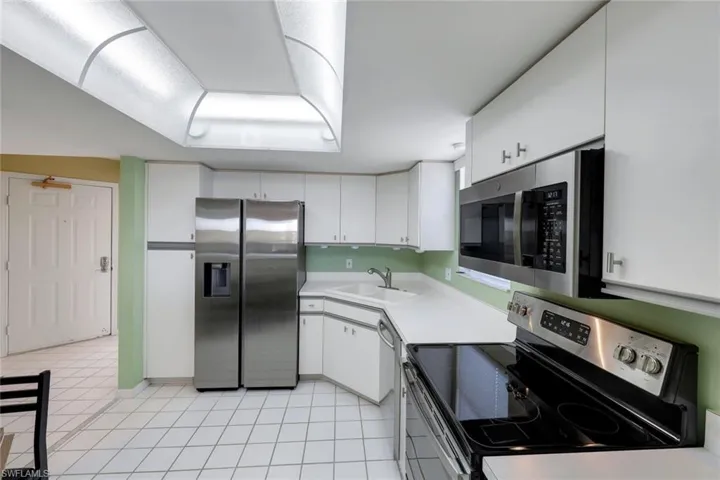 Kitchen featuring stainless steel appliances, light tile patterned flooring, white cabinets, and sink