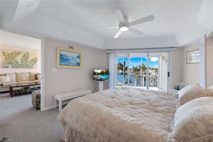 Carpeted bedroom with ceiling fan, access to outside, and a raised ceiling