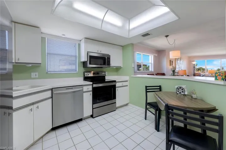 Kitchen featuring stainless steel appliances, light tile patterned floors, pendant lighting, white cabinets, and sink
