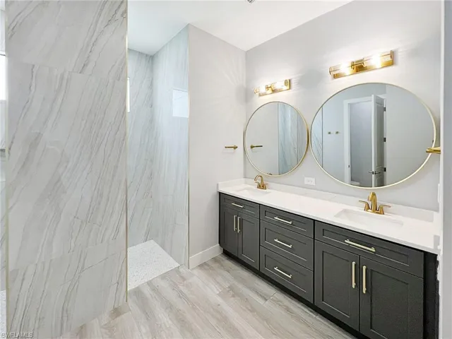 Full bathroom with a marble finish shower, double vanity, and light wood finished floors