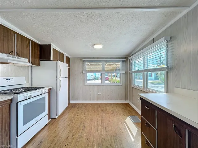 Kitchen with under cabinet range hood, white appliances, light wood-style floors, wood walls, and light countertops