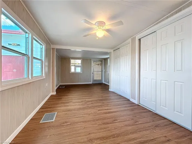 Unfurnished bedroom featuring visible vents, baseboards, two closets, and wood finished floors