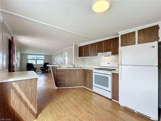 Kitchen with light countertops, a peninsula, light wood-style floors, white appliances, and a sink