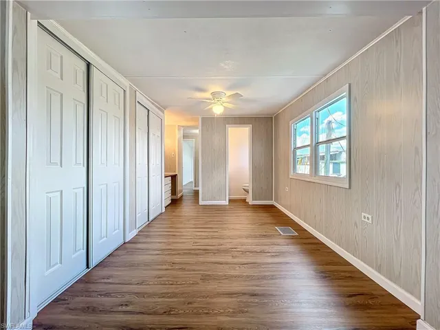 Unfurnished bedroom featuring a ceiling fan, dark wood-style floors, visible vents, baseboards, and multiple closets