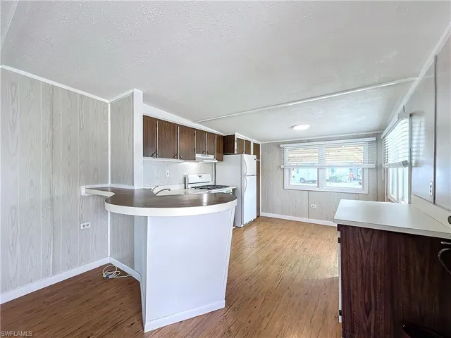 Kitchen featuring dark brown cabinetry, light countertops, a peninsula, wood finished floors, and white appliances