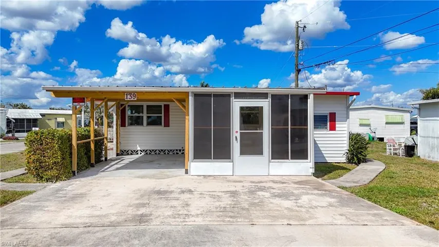 Manufactured / mobile home with an attached carport, concrete driveway, a front lawn, and a sunroom