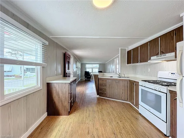 Kitchen with light wood-type flooring, under cabinet range hood, a sink, gas range gas stove, and light countertops