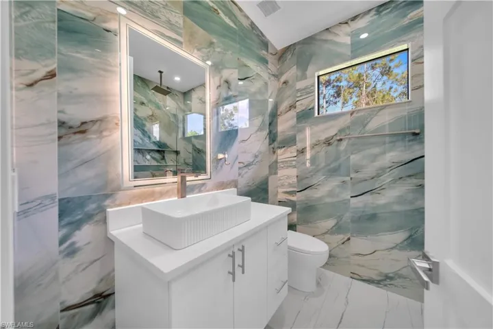 Bathroom with vanity, light marble finish floors, tile walls, and a marble finish shower